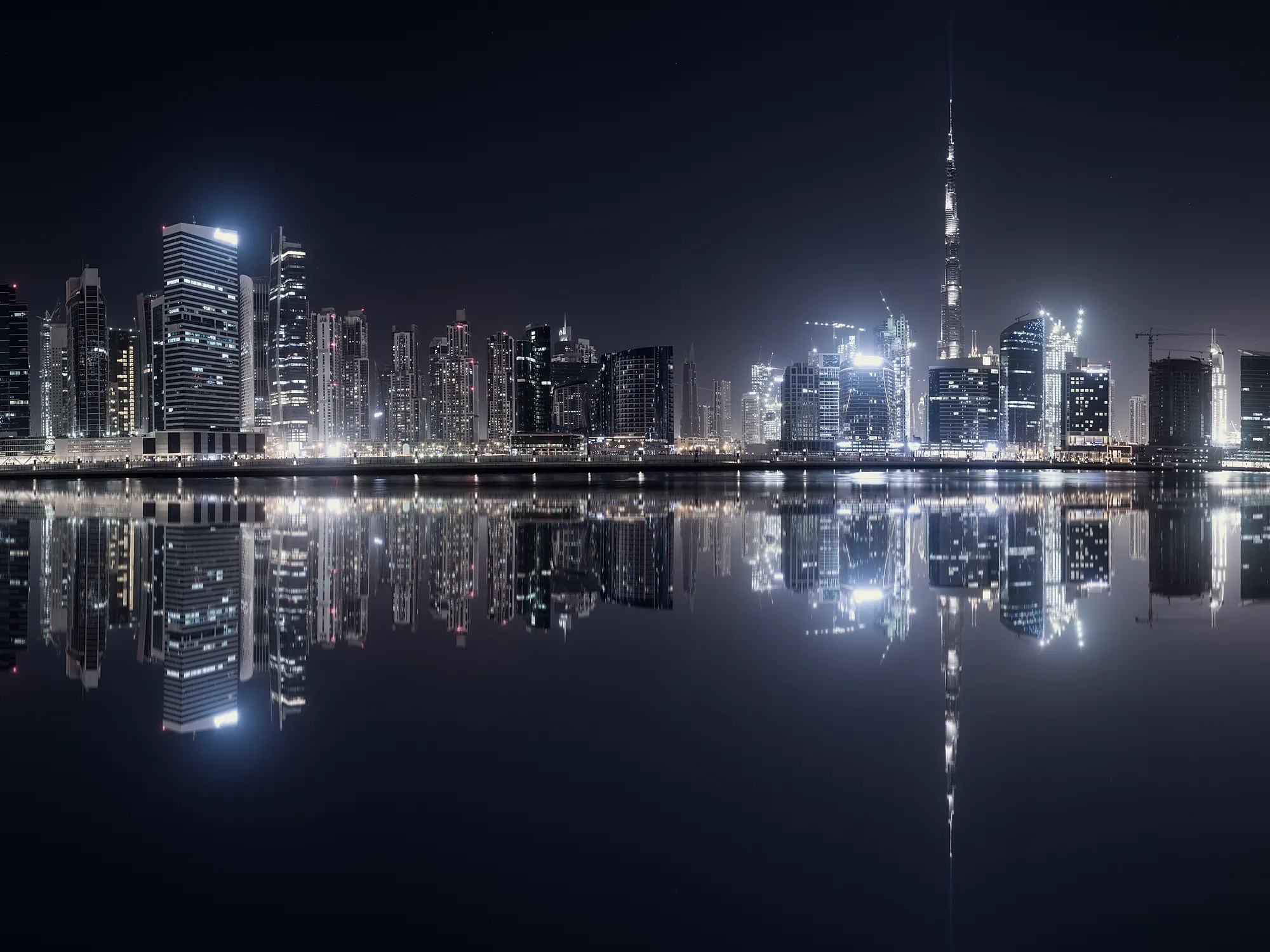 A Gulf financial skyline at night, mirrored in still water.